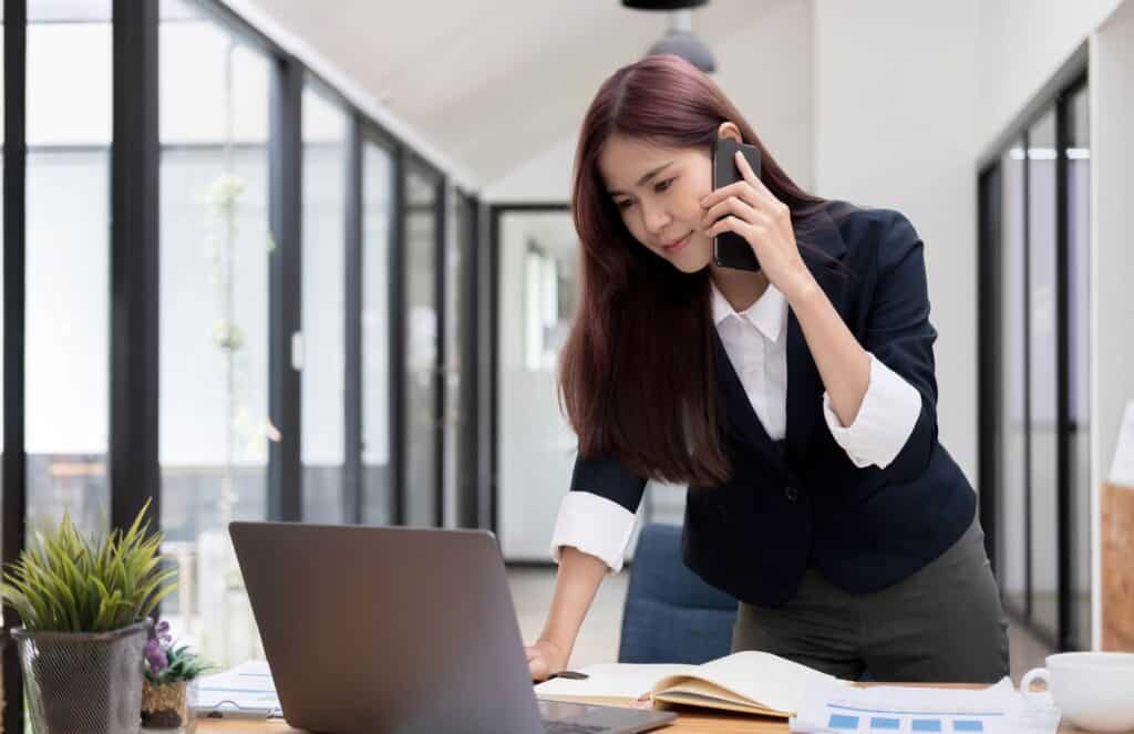 Beautiful attractive young asian businesswoman talking on the phone with her colleague and checking