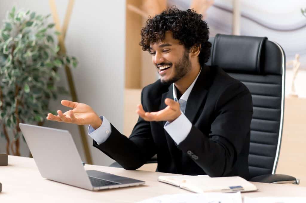 Mann im Anzug lächelt und gestikuliert während eines Online-Meetings – Vertrauen und Beziehung im Resilienzcoaching