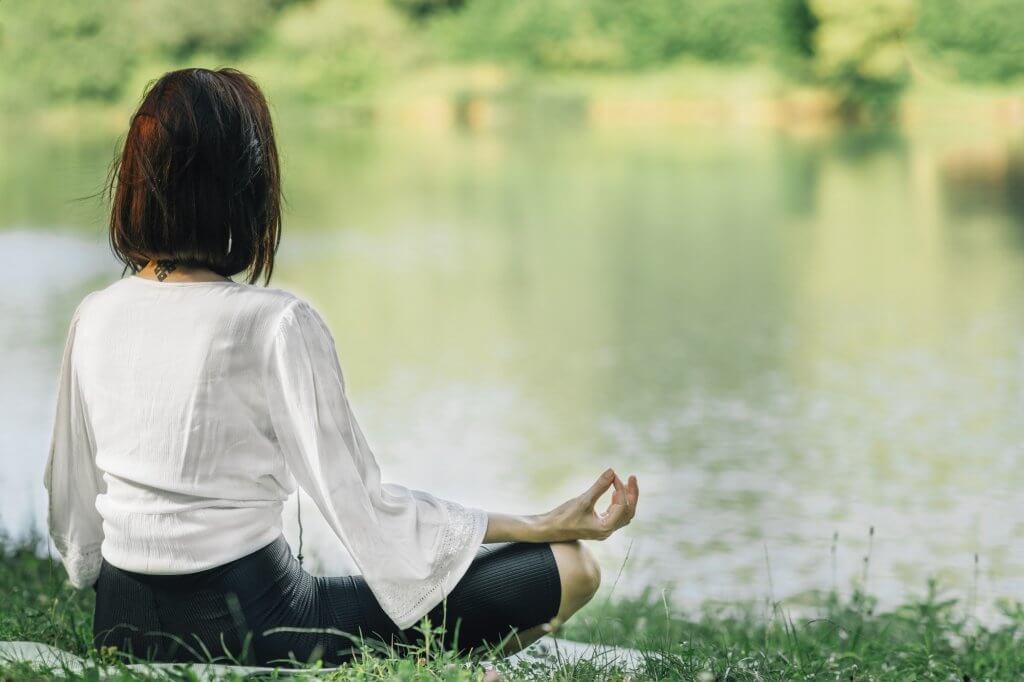 Young Woman Practicing Meditation near Water in the Nature