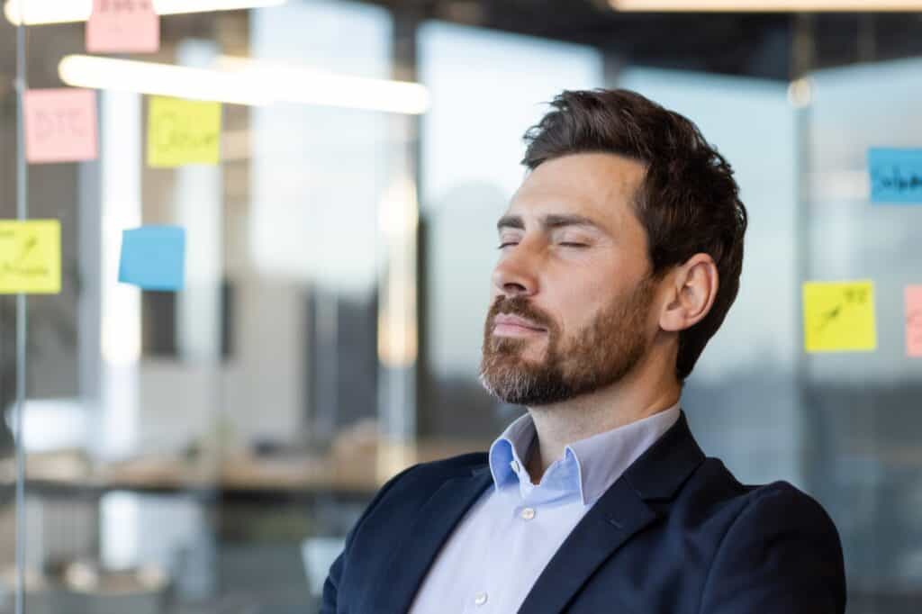 Mann mit geschlossenen Augen bei Achtsamkeitsübung im Büro, farbige Post-its im Hintergrund