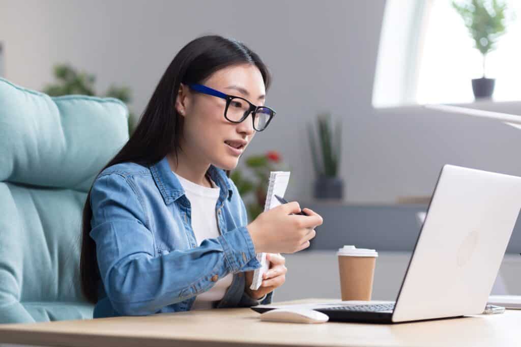 Frau im Homeoffice sitzt mit Kopfhörer und Kaffeetasse vor Laptop und spricht – Symbol für Coaching oder Beratung bei Stress und Burnout